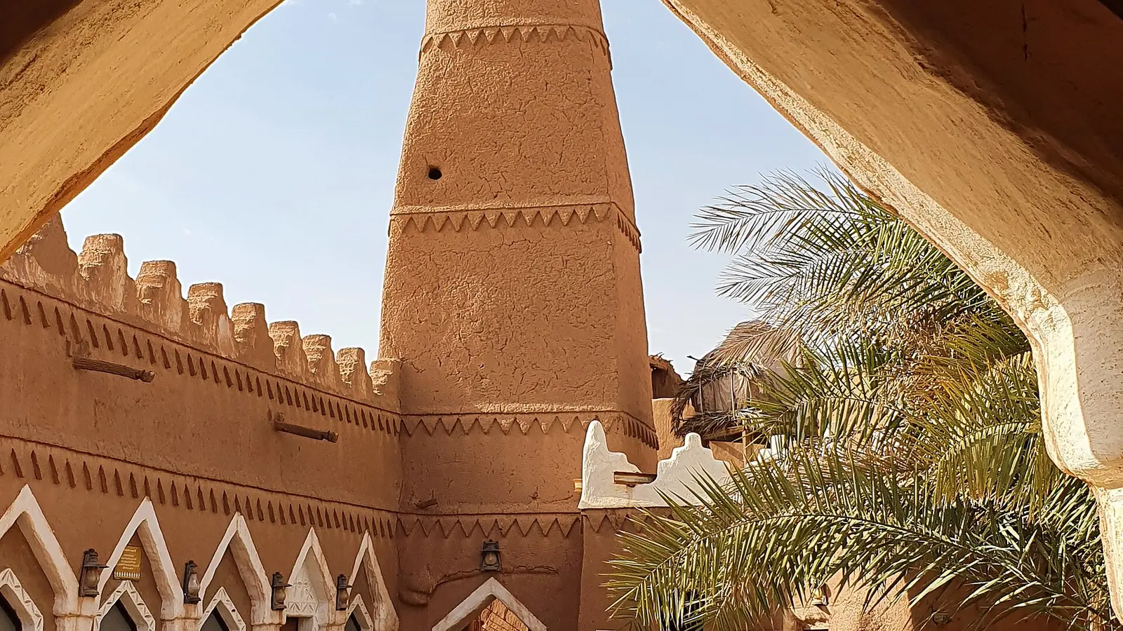 قوس طيني تقليدي يؤطر برج مسجد قديم في بلدة أشيقر التاريخية، عمارة نجدية طينية بلا وجوه أو لافتات