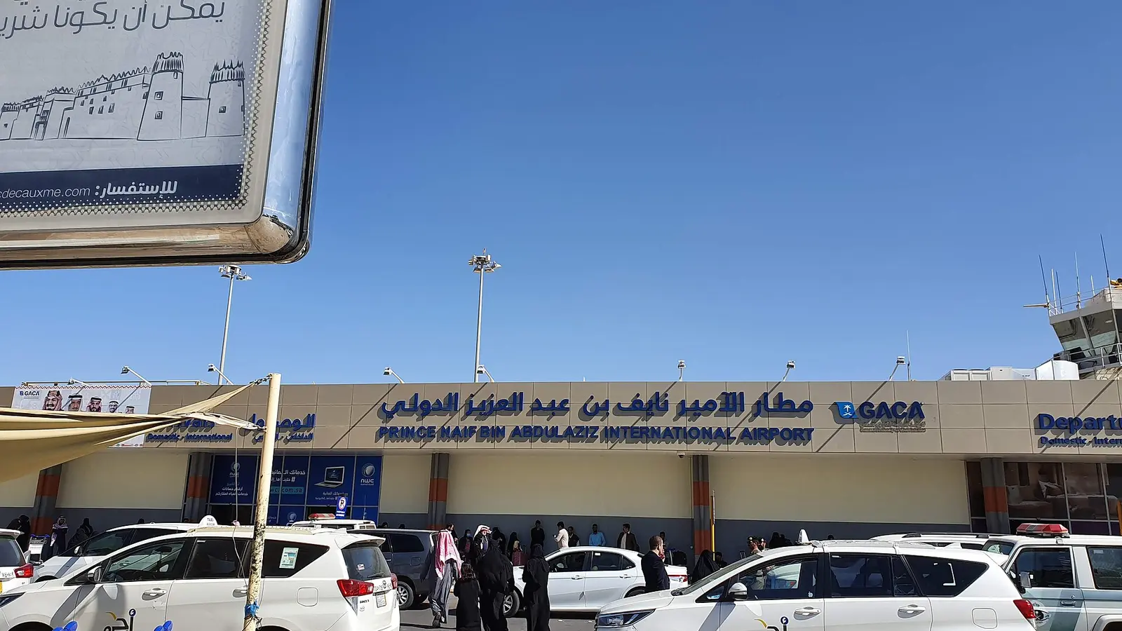 واجهة مطار سعودي بمركبات ومسافرين أمام المدخل، ترمز إلى معاملات حكومية يطلبها أشخاص مختلفون نيابة عن غيرهم