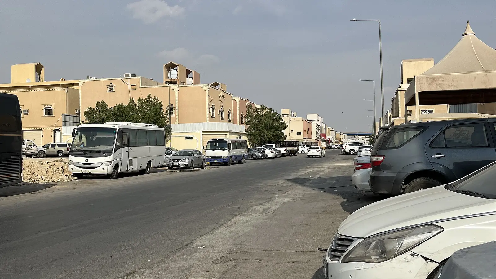 شارع تجاري في حي العزيزية بالرياض تصطف على جانبيه السيارات والمركبات التجارية نهارًا