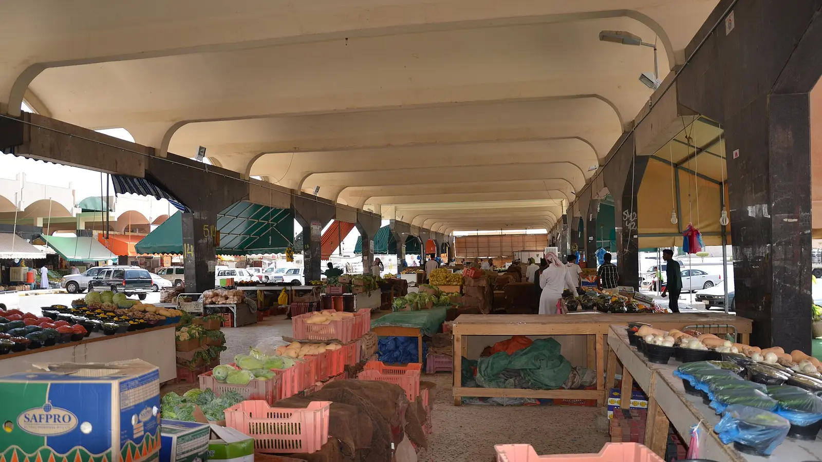 ممرّ مغطّى داخل أسواق الربوة المركزية في الرياض يعرض منتجات طازجة على طاولات ورفوف بلاستيكية، تعبيرًا عن نشاط الأسماء والمحال التجارية في السعودية