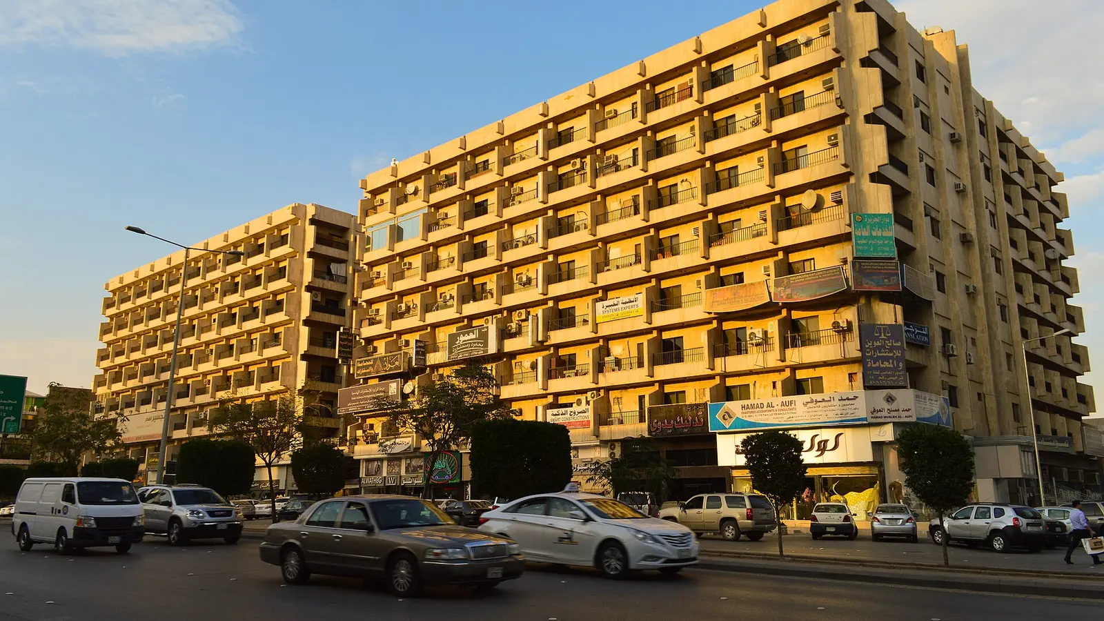 مبنى تجاري بشارع العليا في الرياض بمحلات ولافتات متعددة في الطابق الأرضي ومركبات تسير أمامه