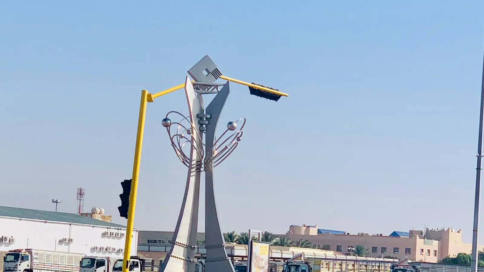 نصب تذكاري حديث في دوار بمدينة حفر الباطن تحيط به مبانٍ ومركبات على الطريق