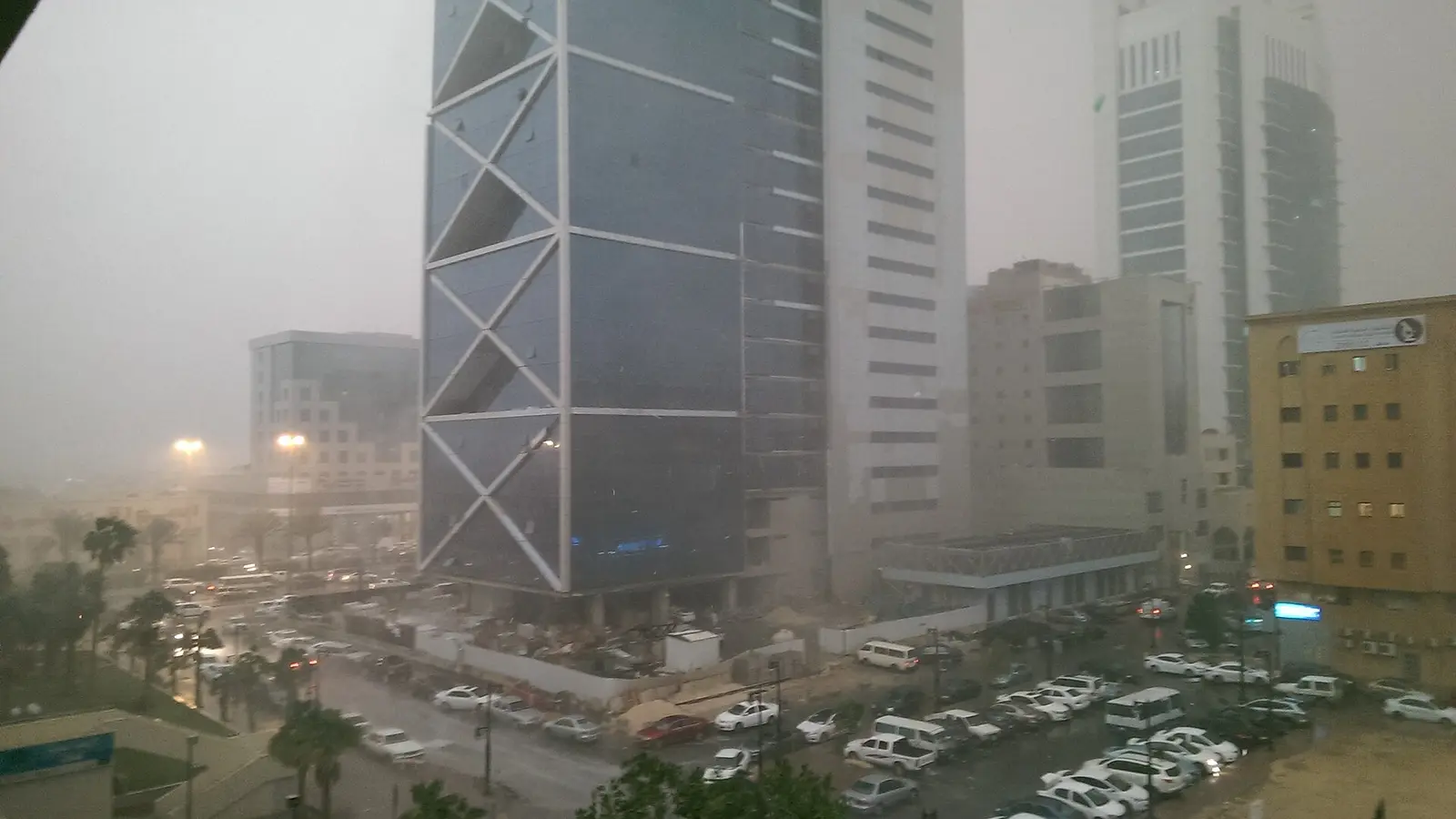 ازدحام مركبات على أحد شوارع الرياض خلال هطول أمطار، بمواقف سيارات ومبانٍ عالية في الخلفية