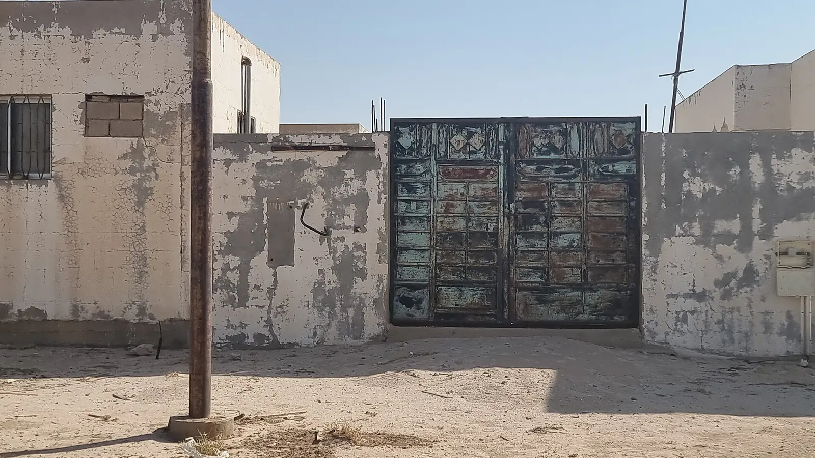 مبنى سكني قديم متهالك بجدران مقشّرة الطلاء وبوابة معدنية صدئة، يوضّح حالة التلف التي تستوجب استخراج رخصة ترميم قبل الإصلاح