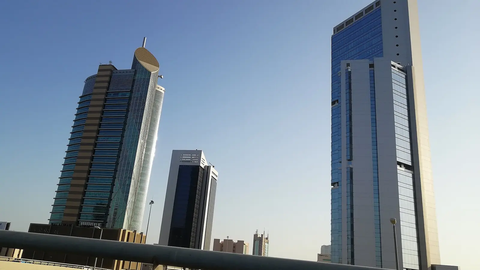 أبراج تجارية ومكتبية حديثة في مدينة الخبر بالمملكة العربية السعودية تحت سماء صافية مع سياج جسر مشاة في المقدمة
