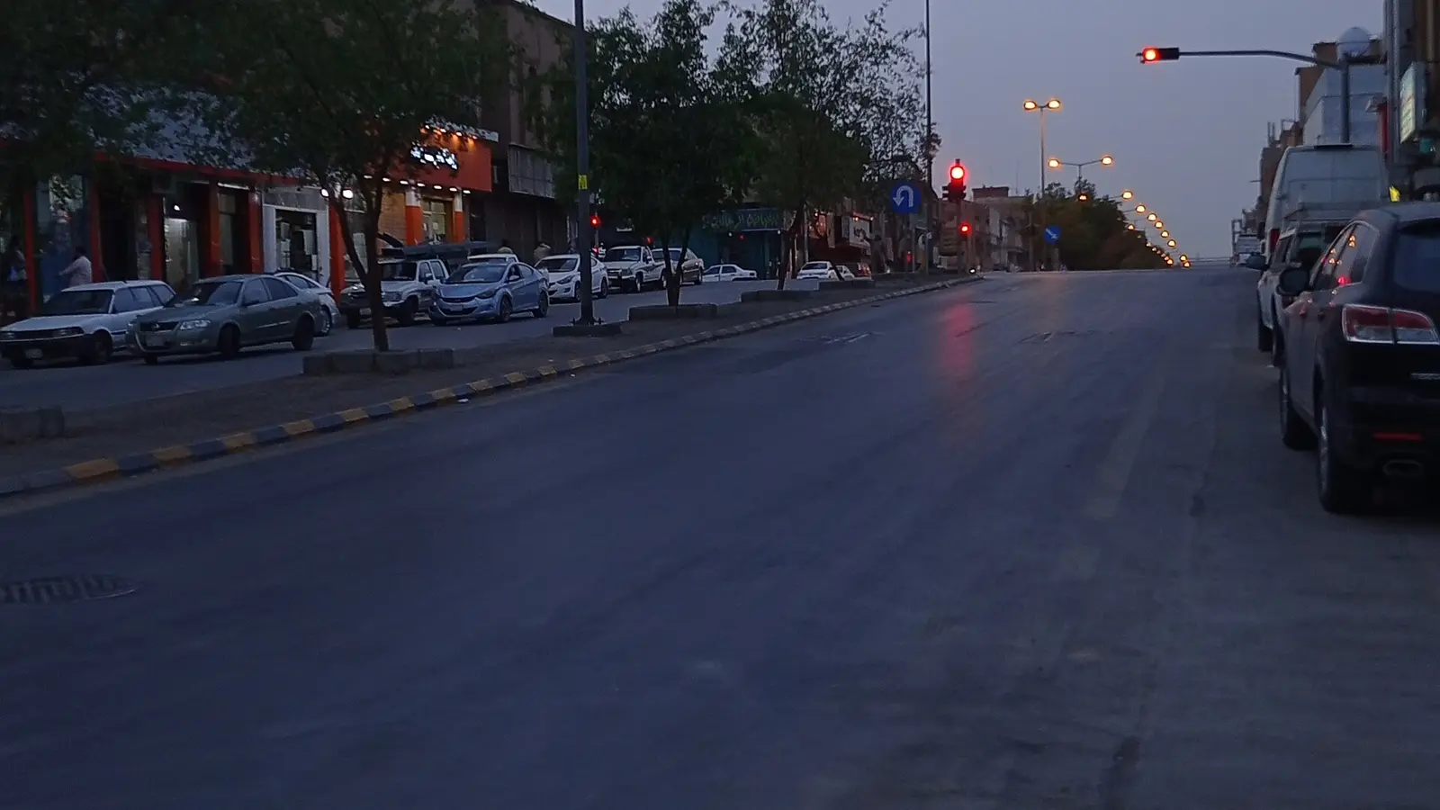 شارع تجاري بحي الخالدية في الرياض عند المغيب، تصطف عليه واجهات محلات ومطاعم صغيرة