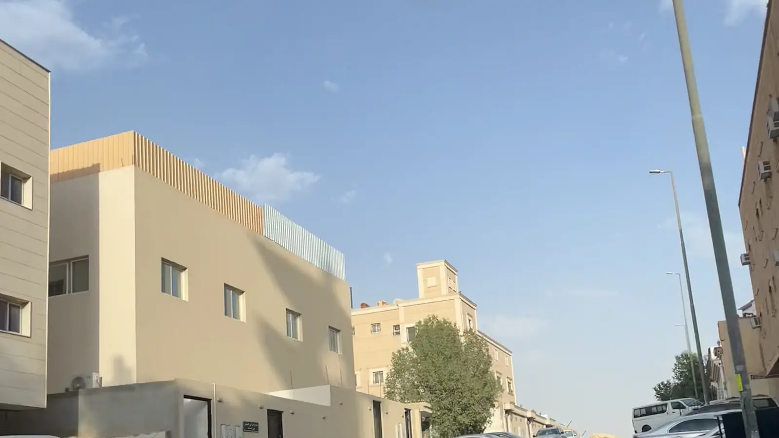 شارع سكني بأحد أحياء الرياض، مبانٍ سكنية ومركبات مصفوفة على جانبي الطريق